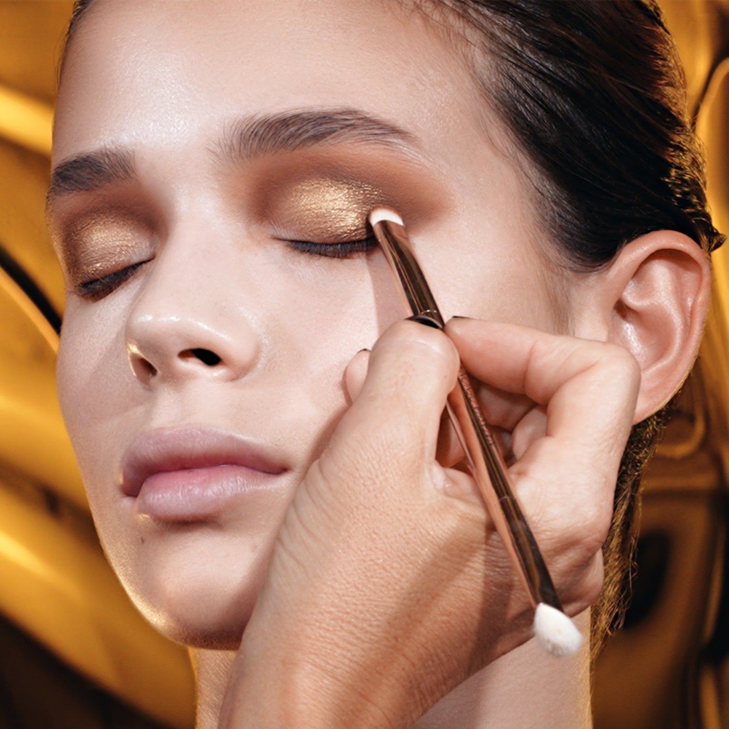 Golden Eyeshadow Palette model look on a gold background. Natasha is applying the eyeshadow on the model's eyelid with a brush. Golden Eyeshadow Palette model look on a gold background. Natasha is applying the eyeshadow on the model's eyelid with a brush.